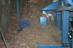 La motorisation de ce transfert à chaînes est composée d’un moteur électrique refroidi par air pulsé, de courroies de transmission de puissance en V, d’un réducteur à vis sans fin refroidi par air pulsé ainsi que d’une chaîne de transmission de puissance entraînant l’arbre de tête. L’absence de déflecteur fait en sorte que la motorisation est littéralement "Enterrée" sous l’amoncellement d’écorces. On constate la surchauffe du moteur électrique et du réducteur qui ne sont plus ventilés ainsi que l’introduction d’écorces au niveau des courroies.